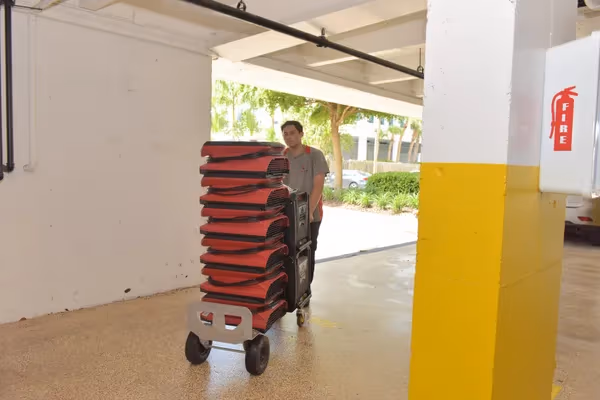Technician pushing a cart loaded with air movers through a parking garage